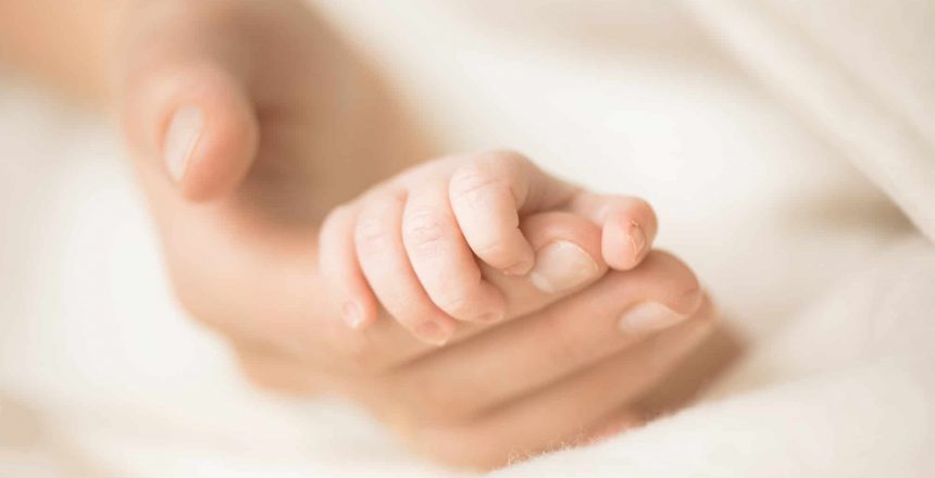 Female hand holding her newborn baby's hand. Mom with her child. Maternity, family, birth